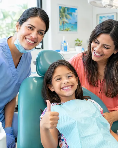Dental assistant, a smiling girl in the dental chair and her mom
