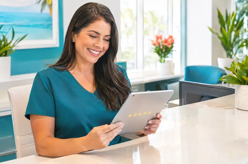 Dental office manager smiling as she reads new reviews on a tablet